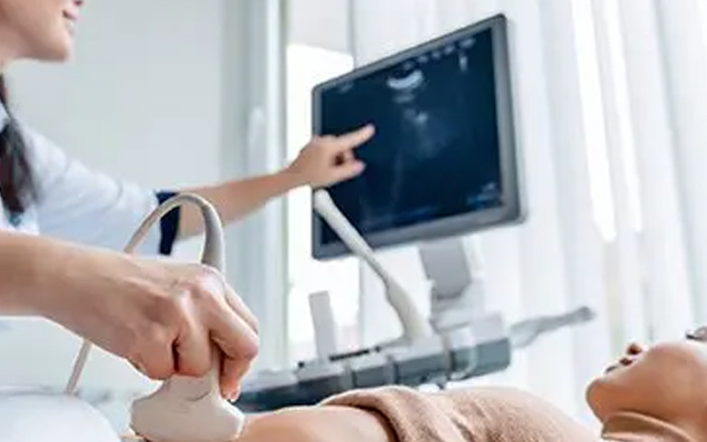 Pregnant woman undergoing a pregnancy ultrasonography test at a clinic, with sonographer pointing at the monitor and using an ultrasound probe.